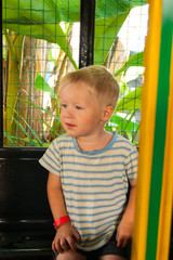 A three-year-old little fair-haired boy rides in a yellow-green children's train in an amusement...