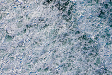 Abstract aerial view of churning blue ocean waves with frothy white foam and swirling patterns near Vestvågøy, Norway.