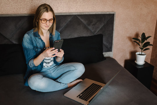 Girl checking social apps in phone in home. Woman working, learns and using laptop computer in the bedroom. Freelancer. Writing, typing. Communication and technology concept.
