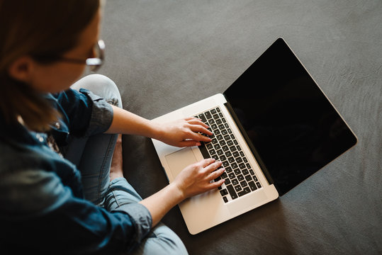 Beautiful young woman working and using black blank screen laptop computer in the bedroom. Freelancer. Writing, typing. Girl in social apps. Communication and technology concept. Top view.