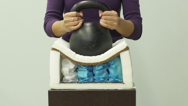 Woman puts a heavy weight on an orthopedic foam mattress with spring slow-mo