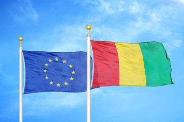 European Union and Guinea two flags on flagpoles and blue cloudy sky