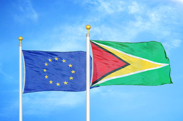 European Union and Guyana two flags on flagpoles and blue cloudy sky