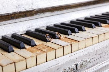 Wedding rings on an old white piano, close-up