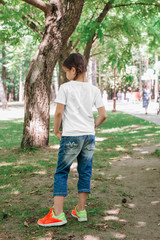 back views of little girl in blank t-shirt walking in park. Mockup for design