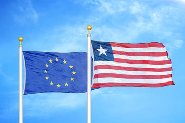 European Union and Liberia two flags on flagpoles and blue cloudy sky