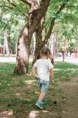 back views of little girl in blank t-shirt walking in park. Mockup for design