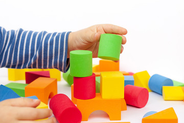A child builds a pyramid of cubes on a white background. The boy's hand holds a cube.