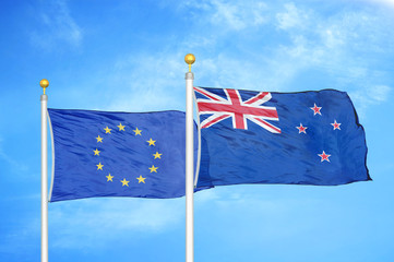 Fototapeta premium European Union and New Zealand two flags on flagpoles and blue cloudy sky
