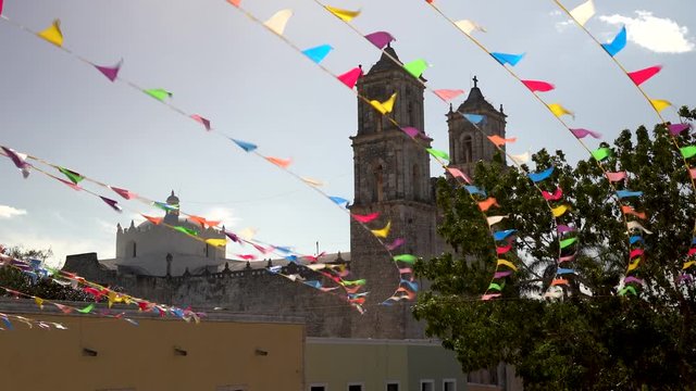 Medium tight closeup of the bell towers of the cathedral San Gervasio with flags waving in Valladolid, Yucatan, Mexico.