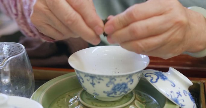 Close up of a person cutting a puer cake piece from Yunnan, using a puer knife and putting it into a gaiwan. Gong fu cha session, a traditional chinese tea discipline. High dynamic range footage.