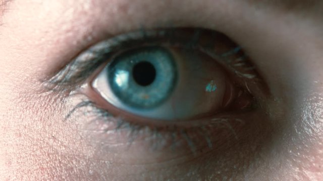 extreme close up of blue eye looking straight into lens with pupil dilating