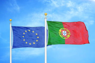 European Union and Portugal two flags on flagpoles and blue cloudy sky