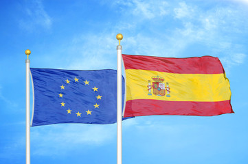 European Union and Spain two flags on flagpoles and blue cloudy sky