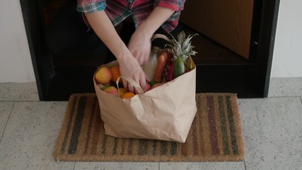 taking grocery bag with fresh fruits from under the door food delivery