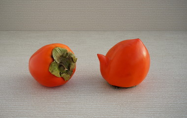 Strange forms of persimmon. Two  ugly shape fruit in the gray background. Funny, unnormal fruit or...