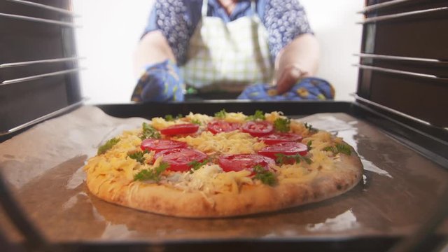 Cooking italian pizza in hot convection oven. Woman chef placing pizza on baking sheet inside hot oven. Frozen pizza topped with tomatoes mozzarella and edam cheese. Interior of electric cooker