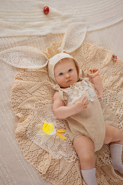 Happy child girl in a costume Easter bunny rabbit with ears and and multicolored eggs lies on a bed in lace and smiling