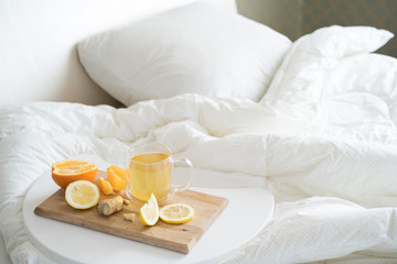 Fototapeta na wymiar Cup with antipyretic drugs for colds,flu.Tea with citrus vitamin C,ginger root,lemon,orange.Wooden tray in patient's bed. Home self-treatment.Medical quarantine antiviral covid-19 coronavirus therapy