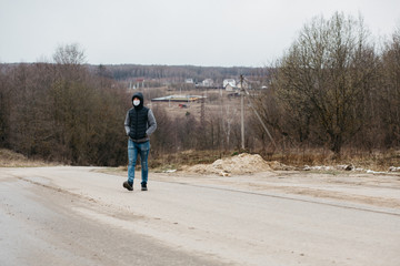 Obraz premium A man in a protective medical mask - modern measures of protection against coronovirus in quarantine conditions. A young man in casual style walks along an empty road