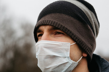 A man in a protective medical mask - modern measures of protection against coronovirus in quarantine conditions. A young man in casual style walks along an empty road