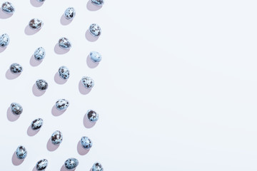 Minimal Easter pattern background in classic blue color with hard light and harsh shadows. Easter flat lay with quail painted eggs, feathers and flowers, copy space, creative card