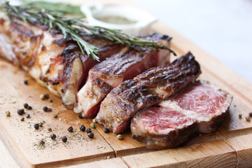 Tomahawk beef steak grilled with spices and rosemary on a wooden board on a light background. Slices of meat. Background image, copy space