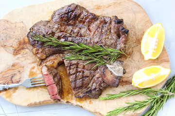 Marble beef grilled with lemon and rosemary on a wooden board on a light background. Slice of meat with a fork. Background image, copy space