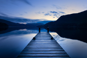 Wooden Jetty/Pier Leading Out To Calm Lake With Reflections At Blue Hour In The Lake District, UK.