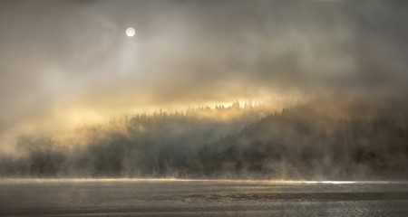 Hidden light behind mist over mountain lake and forest - 335284663
