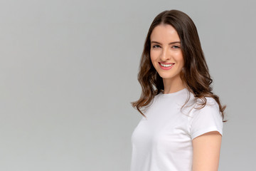 Close up portrait of smiling young woman in white t-shirt looking at camera, isolated on gray background
