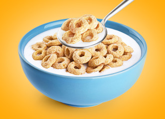 Bowl and spoon with corn rings, milk, yogurt on orange background.