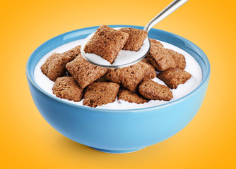Bowl and spoon with chocolate corn pads, milk, yogurt on orange background.
