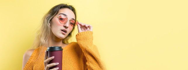 Glamor woman in glasses in an orange sweater with a drink of coffee on a yellow background