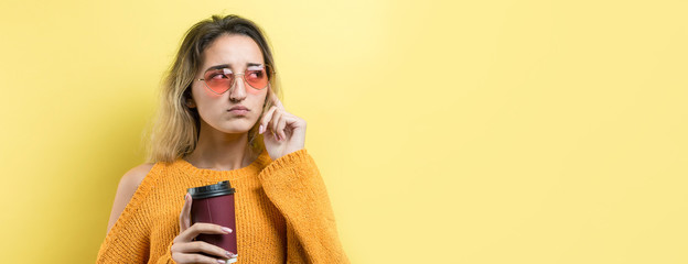 Glamor woman in glasses in an orange sweater with a drink of coffee on a yellow background