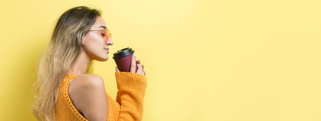Glamor woman in glasses in an orange sweater with a drink of coffee on a yellow background