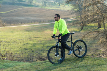 Obraz premium Cyclist in pants and green jacket on a modern carbon hardtail bike with an air suspension fork. The guy on the top of the hill rides a bike.