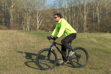 Obraz premium Cyclist in pants and green jacket on a modern carbon hardtail bike with an air suspension fork. The guy on the top of the hill rides a bike.