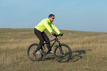 Obraz premium Cyclist in pants and green jacket on a modern carbon hardtail bike with an air suspension fork. The guy on the top of the hill rides a bike.