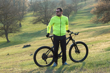Obraz premium Cyclist in pants and green jacket on a modern carbon hardtail bike with an air suspension fork. The guy on the top of the hill rides a bike.