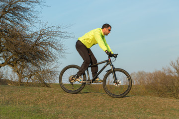 Naklejka premium Cyclist in pants and green jacket on a modern carbon hardtail bike with an air suspension fork. The guy on the top of the hill rides a bike.