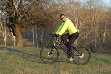 Fototapeta na wymiar Cyclist in pants and green jacket on a modern carbon hardtail bike with an air suspension fork. The guy on the top of the hill rides a bike.