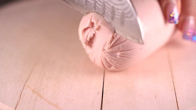 Fleischwurst mit Messer auf einem Schneidebrett in dicke Scheiben schneiden