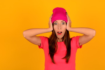 surprised woman in pink hat and t-shirt holding her head on a yellow background portrait