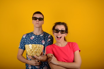 young couple in colored t-shirts with popcorn in cinema on a yellow background