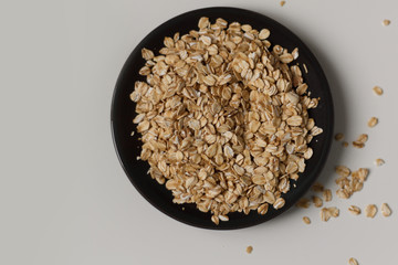 close-up of raw oatmeal on a black plate on a light background. vegetarian food.