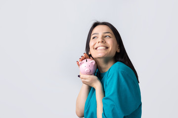 Fototapeta na wymiar The girl holds a pink piggy bank and a coin in her hands. The concept of wealth and accumulation.
