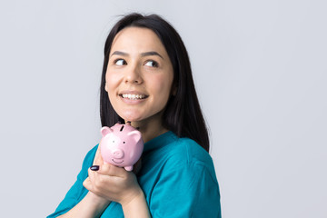 The girl holds a pink piggy bank and a coin in her hands. The concept of wealth and accumulation.