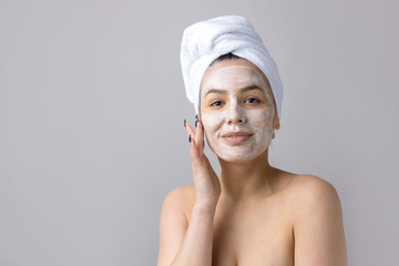 Beauty portrait of woman in white towel on head applies cream to the face. Skincare cleansing eco organic cosmetic spa relax concept.