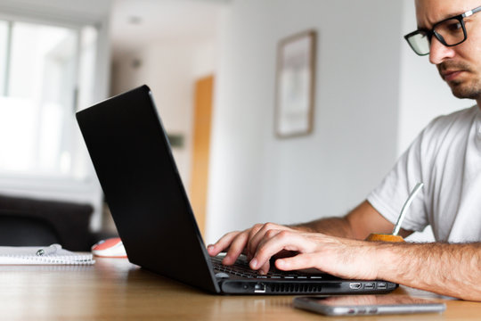 Young Man Telecommuting From Home. Typing A Computer